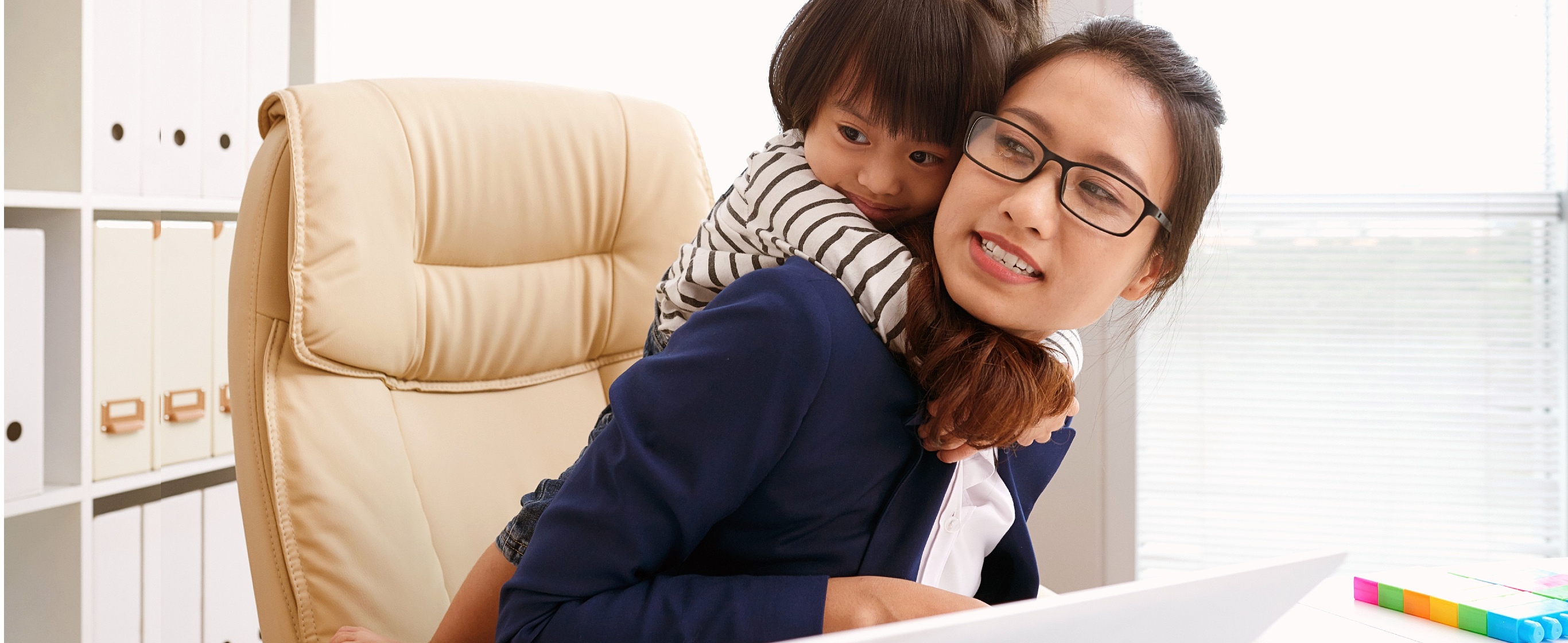 Woman working on laptop, with child on shoulder